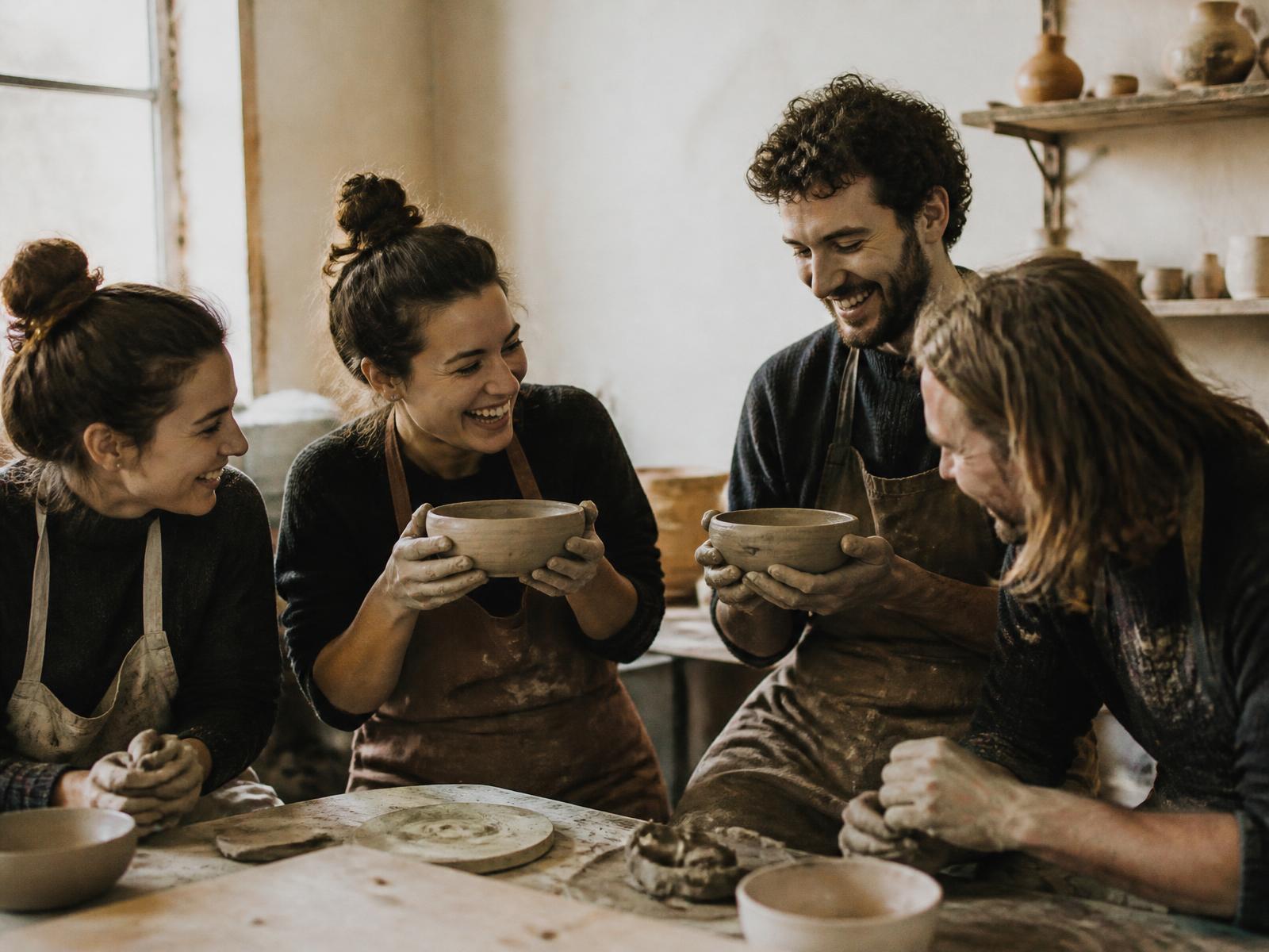 Four adults comparing the bowls they have just thrown at a pottery workshop table