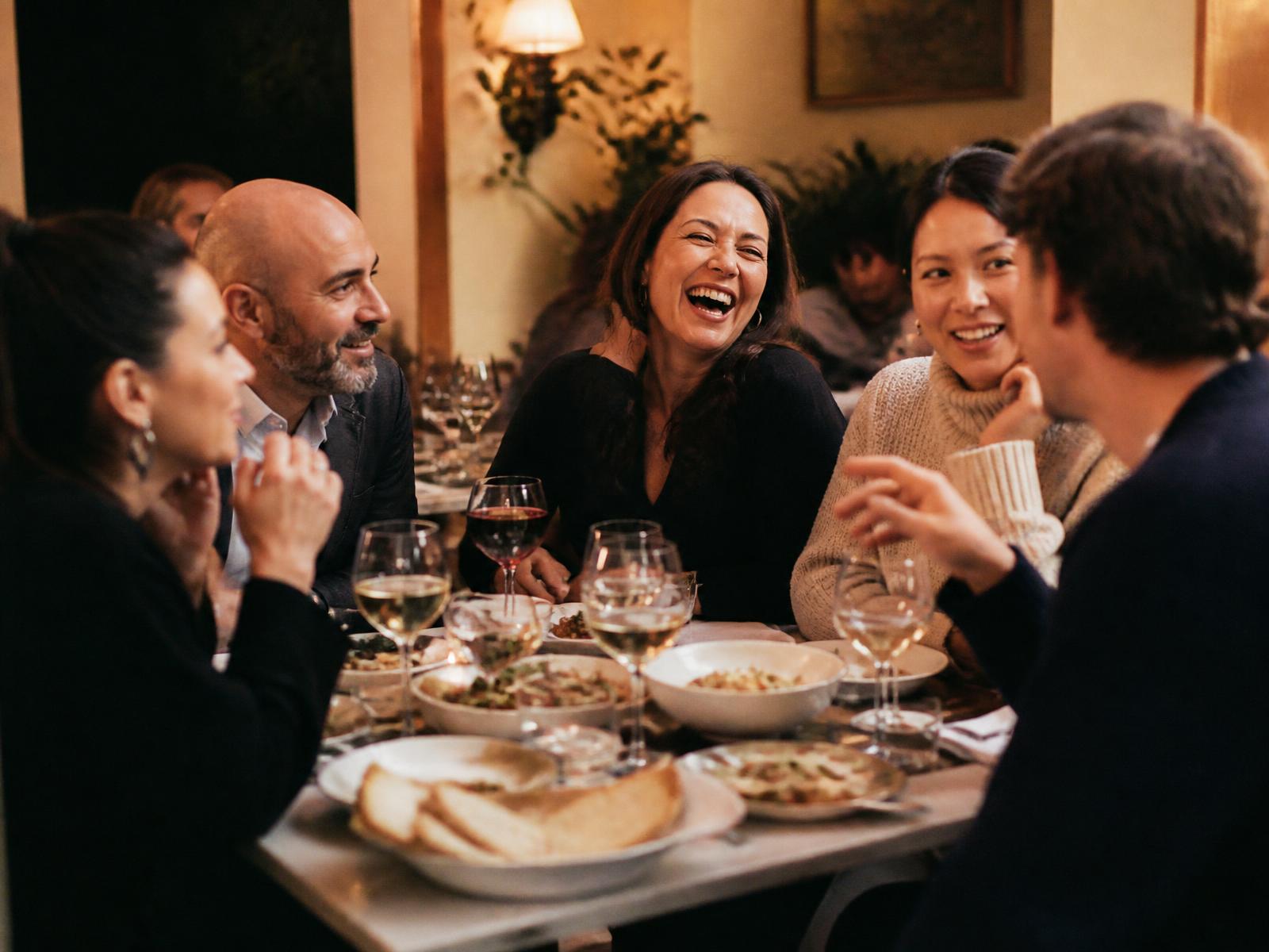 Five adults sharing plates and conversation at a warmly lit neighbourhood restaurant table