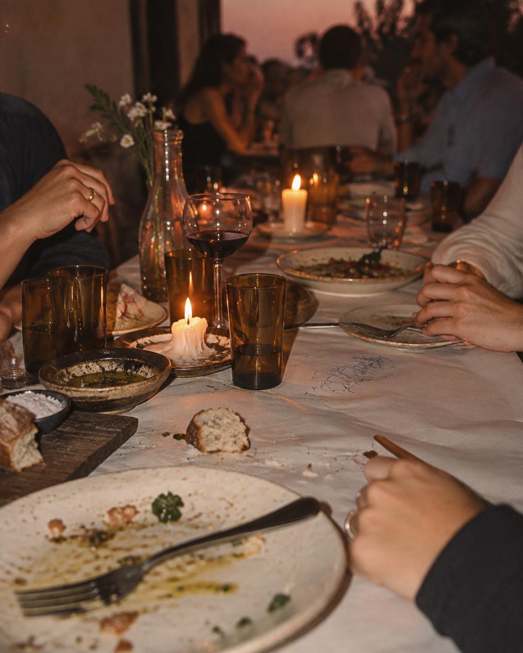 Hands resting on a candlelit dinner table after a shared meal at dusk